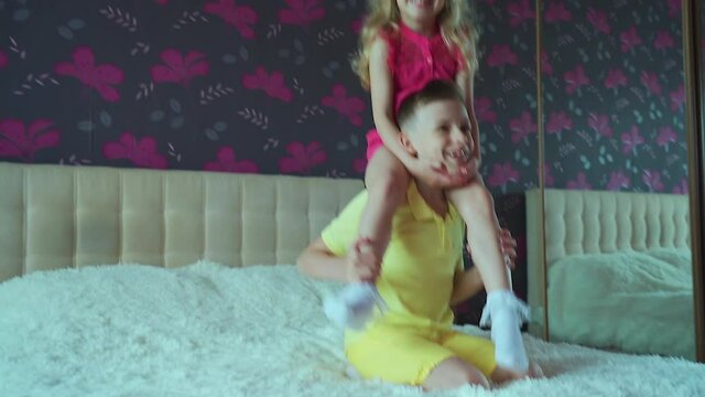 A little girl interferes with homework the boy. Books are lying on the bed.Children have play in bed, the boy tickles the girl and laughs.