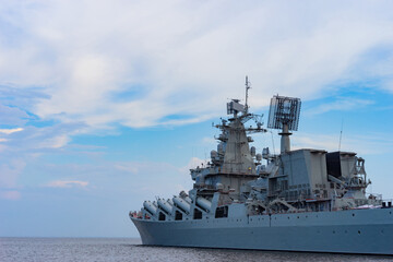 Military cruiser on the background of blue sky. Warship rides on the sea. The missile cruiser sets...