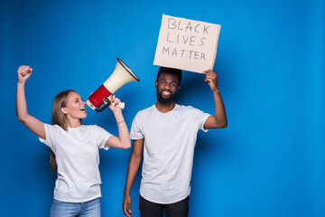 Young caucasian white woman with megaphone and African black man holding a cardboard poster with...