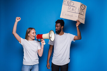 Young caucasian woman with megaphone and African man holding a cardboard poster with the message...