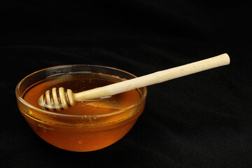 Honey in a bowl with a wooden stick on a black background
