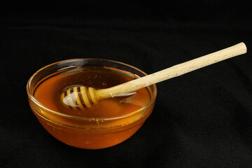 Honey in a bowl with a wooden stick on a black background