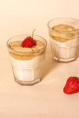 Dalgon coffee in a transparent glass with milk on a pastel background with strawberries. Vertical orientation