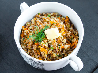 Porridge with vegetables in a white bowl. Garnished with a sprig of parsley. Buckwheat with onions and carrots