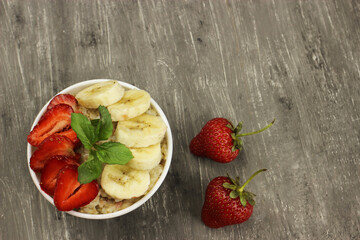 Bowl of oatmeal with a banana, strawberries and mint on a gray background. The view from the top. Fresh healthy Breakfast