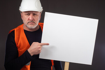 Builder points a finger at the banner. Man in an orange vest. Builder with a poster on a dark...