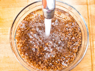 Wash buckwheat in water. Unfinished buckwheat grains are washed under running water. Top view, bubbles