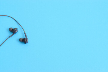 Black earbuds on light blue colorful monochrome background with copy space for text 