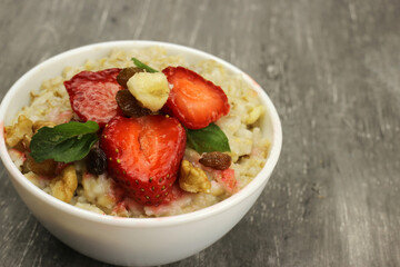 Bowl of oatmeal with a banana, strawberries and mint on a gray background. Fresh healthy Breakfast