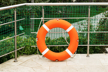A round orange rescue buoy stands on land near a metal ladder.