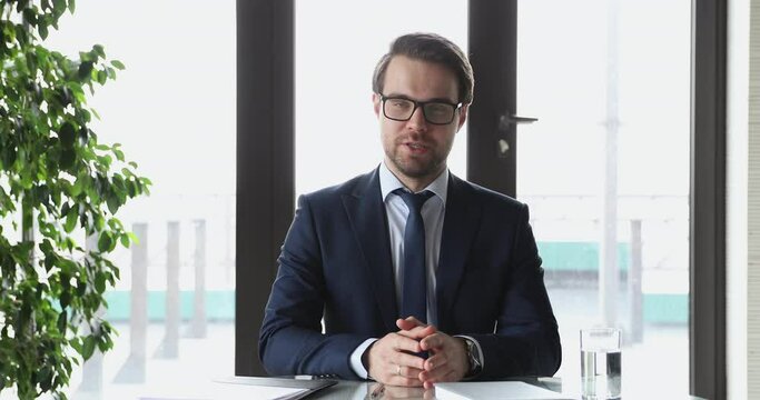 Confident businessman wearing suit speaking to camera recording business video presentation. Male ceo talking to webcam broadcasting webinar, streaming webcast training, conference calling in office.