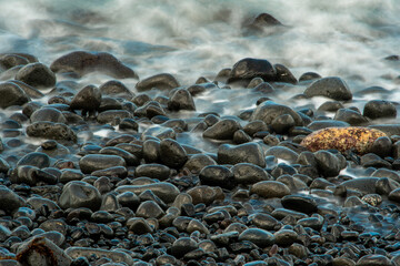 Waves crashing on pebble beach with slow shutter speed. Artistic effect.