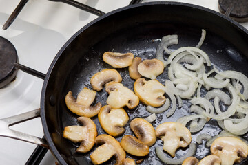 Fried sliced champignons with onions in a pan. Mushrooms with onions in a pan. Cooking lunch and dinner. Fried onion rings