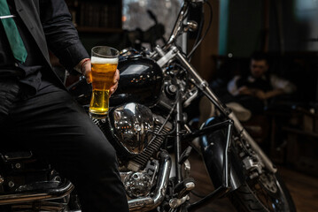 Biker sitting on a custom motorcycle with a glass of shiny craft beer. Chrome bike