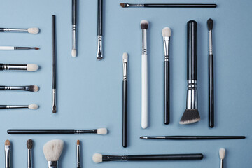 brushes for make-up or drawing white and black of different sizes lie in different directions on a blue background.