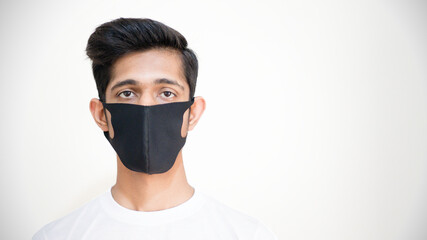 Young brown asian boy wearing black cloth mask to protect himself from the viral flu and disease corona virus covid 19 standing in one side of the frame rule of third posing, selective focus