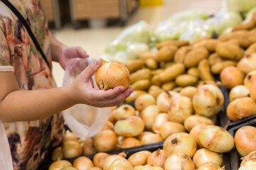 Hand choosing fresh onion from a basket in supermarket. Healthy lifestyle. A young woman chooses...