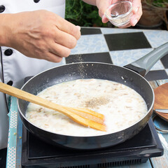 Chef putting pepper in the pan for cooking mushroom cream soup