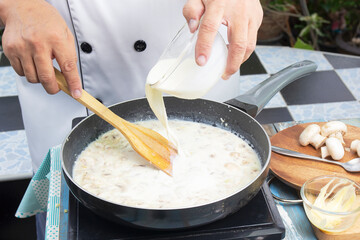 Chef pouring whipping cream in the pan for cooking mushroom cream soup