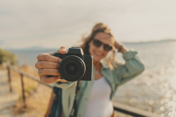 Obraz premium Close-up photo camera in the hand of a happy traveler woman by the sea, joy of vacation and travel