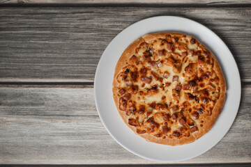 Pizza with bacon, chicken and melted cheese on wood table.