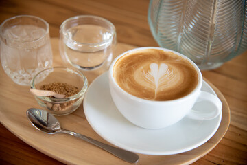 A cup of hot latte with latte art with sugar and a glass of water on wood table.