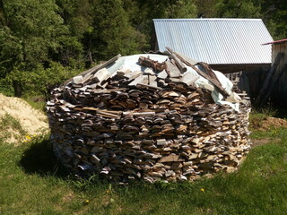 Round woodpile. This can still be found in the Russian outback. Green grass. The trees. The roof of the house under a metal roof.