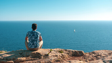Young man sitting at the sea on the horizon
