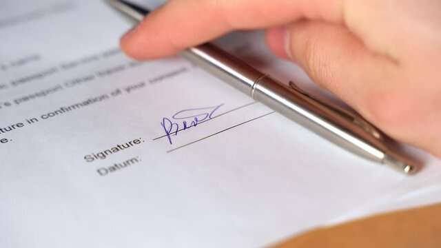 Person signs the document and puts the pen. Man's hand signed the contract by pen and put pen on table. Businessman is signing a contract on white papper. Closeup macro shot. Signature Is Fake