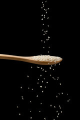 Sprinkle white sesame seeds onto a wooden spoon. Flowing sesame on black background.