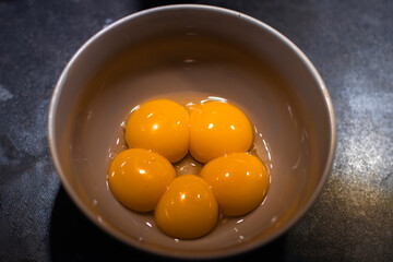 Five egg yolks in a bowl on black kitchen top
