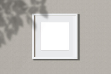 Minimal empty square white frame picture mock up hanging on white wall background with leaves...