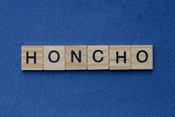 Fototapeta premium tekst na szarym słowie honcho małymi drewnianymi literami z czarną czcionką na niebieskim tle
