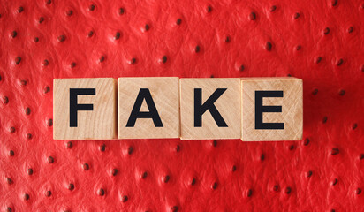 FAKE word written in wooden blocks on red leather. Fake or real news, myth or true concept