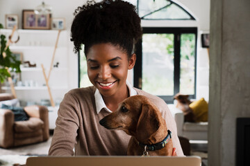 Beautiful mixed race woman working from home on her laptop with dog on her lap