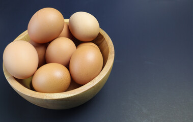 Chicken eggs in a wooden bowl on a black background