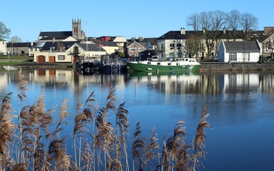 Fototapeta na wymiar Carrick-on-Shannon, County Leitrim, Ireland viewed from across River Shannon against backdrop of blue sky on winter day