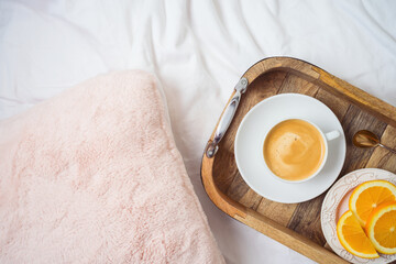 Coffee cup and fresh oranges on wooden tray on morning bed background. Top view from above