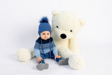 a smiling little boy is sitting in Winter clothes with a large Teddy bear