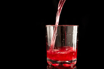 A glass filled with red juice on a black background