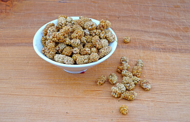 Plateful of Organic dried mulberry and Spilled dried mulberry on Wooden Background