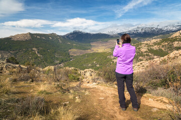 Naklejka premium Young girl dressed in a purple fleece makes photographs of a mountain landscape with her mobile phone
