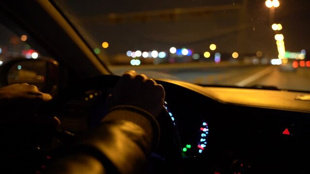 Man Driving Car hrough streets of night city. Close-up of a man hands lie on the steering wheel of a car. Glare in the window of the car