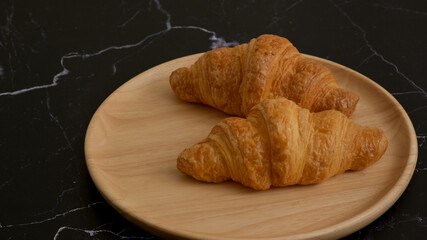 Freshly baked croissants on wooden plate, dark stone background