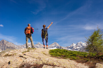 Fototapeta premium Couple with backpack on mountain top. Two people looking at scenic alpine landscape summer vacation fitness wellbeing freedom concept