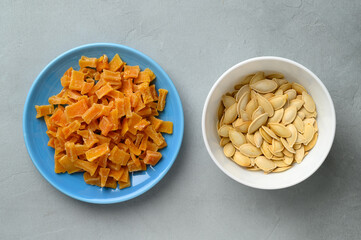 Dried pumpkin slices and seeds in bowls on a gray stone background. Candied pumpkin. Top view.