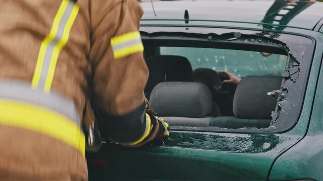 Car accident rescue, firefighter breaking the glass on the car to reach injured person. Close up, Slow motion shot.