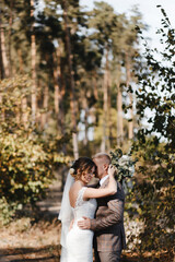 Bride and groom embracing each other at the background of the trees in the forest. Bride and groom portrait