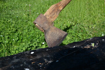 Close-up of an old axe with a wooden handle stuck in a charred oak log.