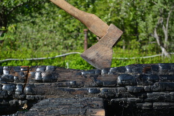 Close-up of an old axe with a wooden handle stuck in a charred oak log.
